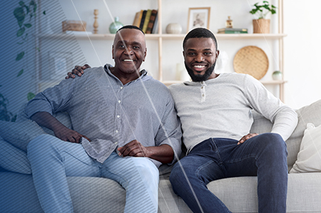 Younger man with his arm around older man sitting on a couch